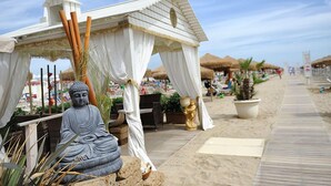 A beach with a white gazebo, a Buddha statue, and thatched umbrellas. - Hotel Thea (Gabicce Mare)