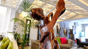 A modern living room with a large wooden sculpture, a sofa, and a potted plant. - Hotel Thea (Gabicce Mare)