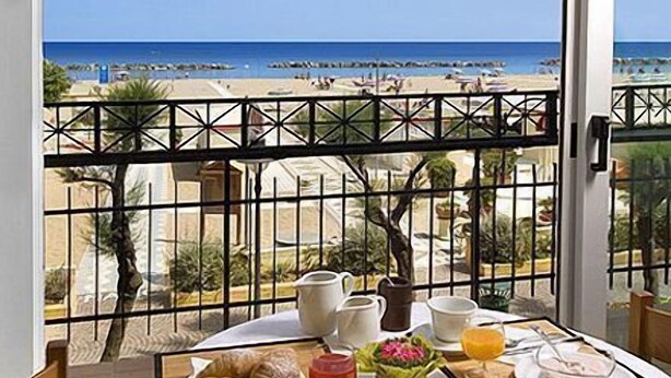 A balcony table with breakfast items and a view of the beach. - Hotel Thea (Gabicce Mare)