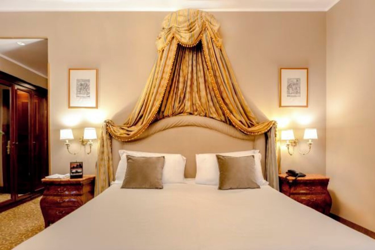 A large bed with a canopy, two bedside lamps, and framed pictures on the walls.