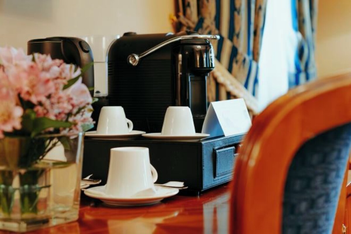 A coffee maker, two cups, and a vase with flowers on a table.