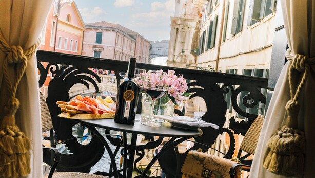 Un balcon avec une table dressée pour un repas, comprenant une bouteille de vin, un verre de vin et une assiette de nourriture.
