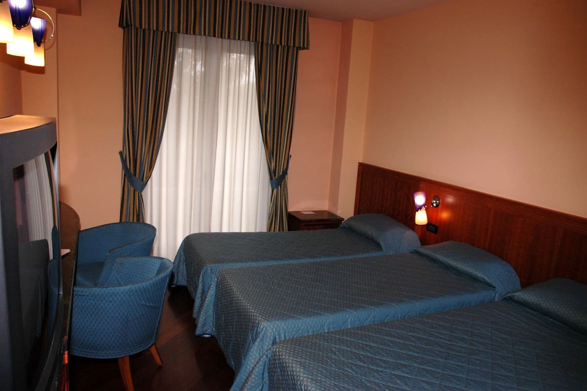 A hotel room with two beds, a chair, a desk, and a lamp.
