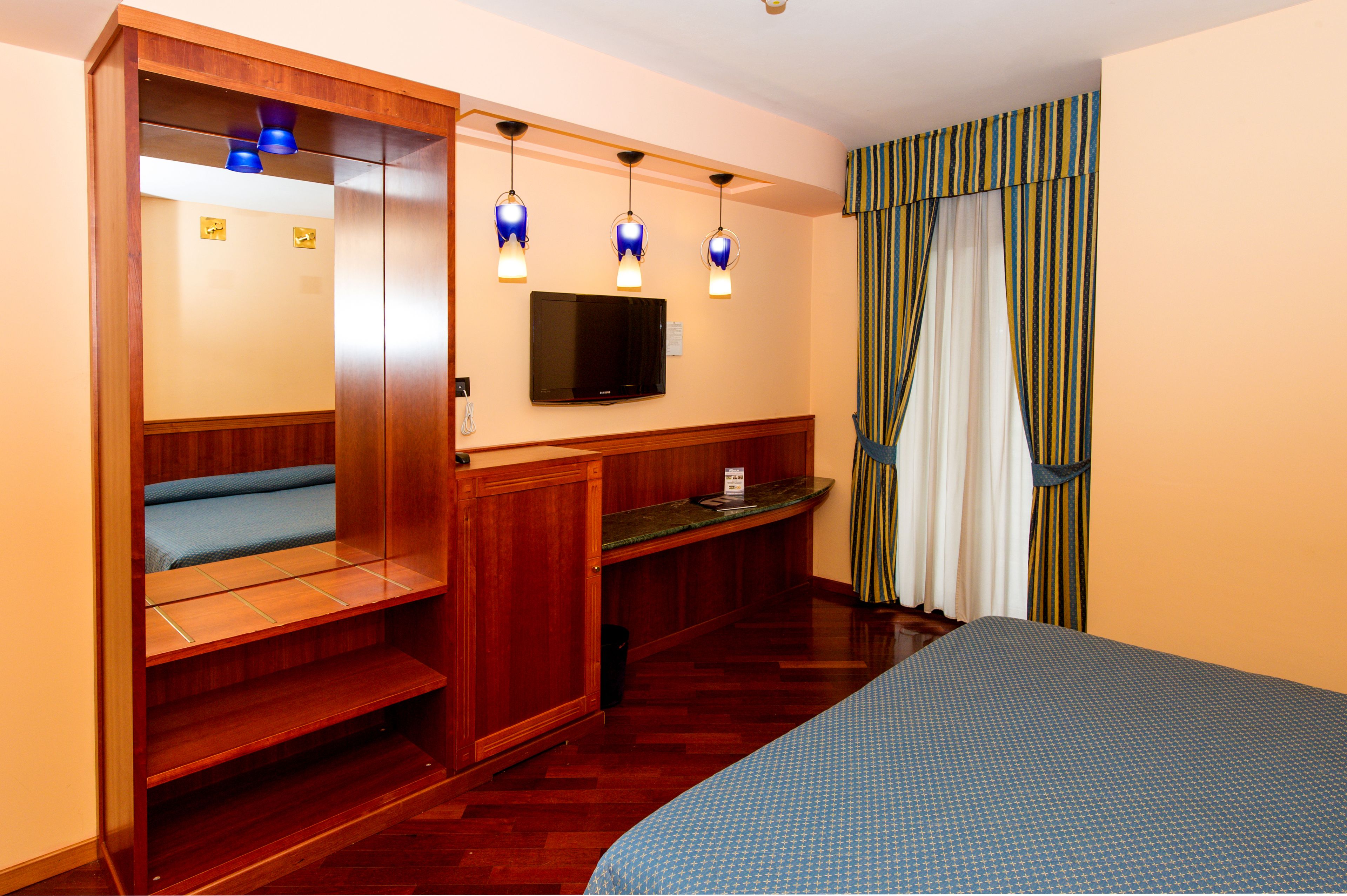 A hotel room with a bed, a seating area with a bench, a television, and a desk.