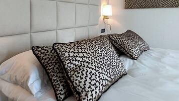 Ett hotellrum med en stoppad sänggavel, mönstrade kuddar, en vägglampa och en dekorativ väggdekoration.