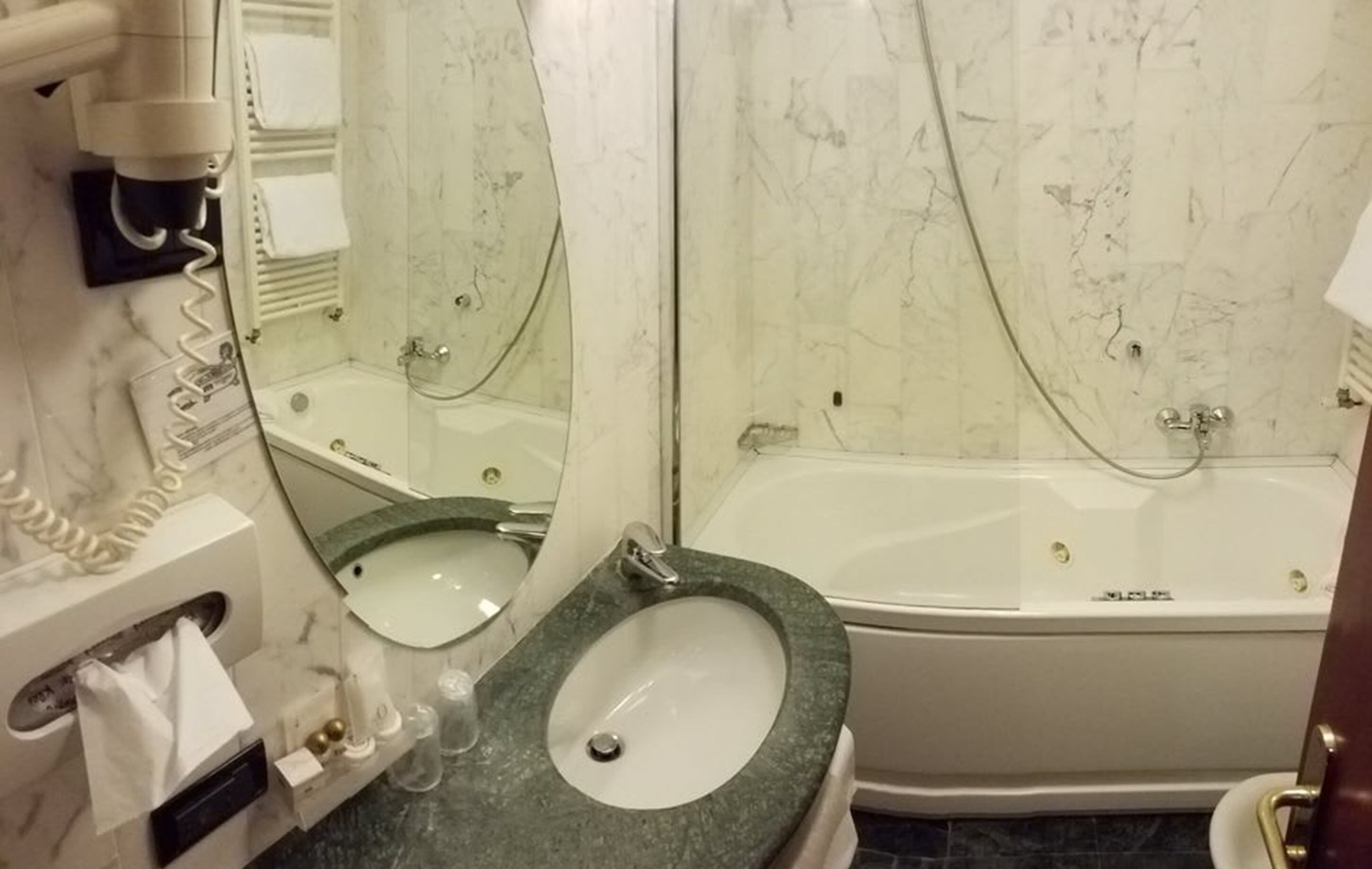 A bathroom with a marble wall, a sink, a bathtub, and a mirror.