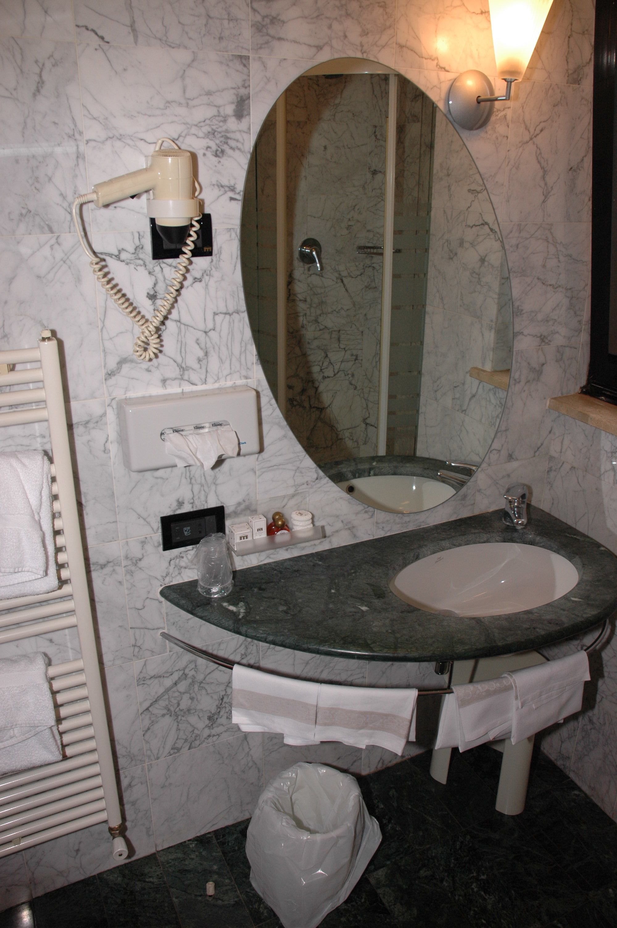 Un baño con lavamanos de mármol, un espejo grande, un secador de pelo y un perchero para toallas.