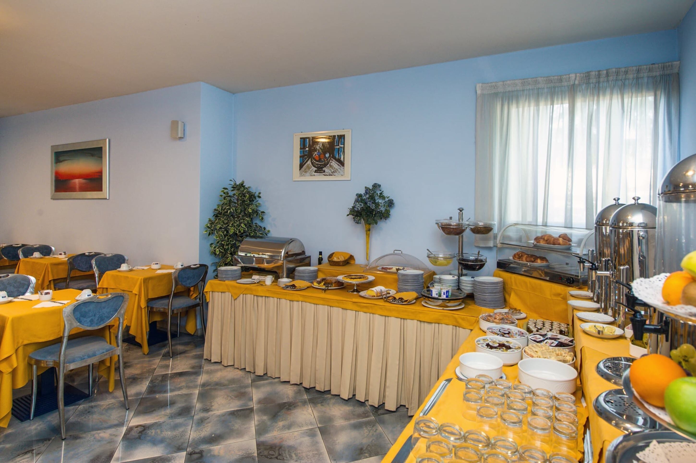 Comedor con mesas preparadas para el desayuno, que incluye un bufé con diferentes alimentos y una estación de café.