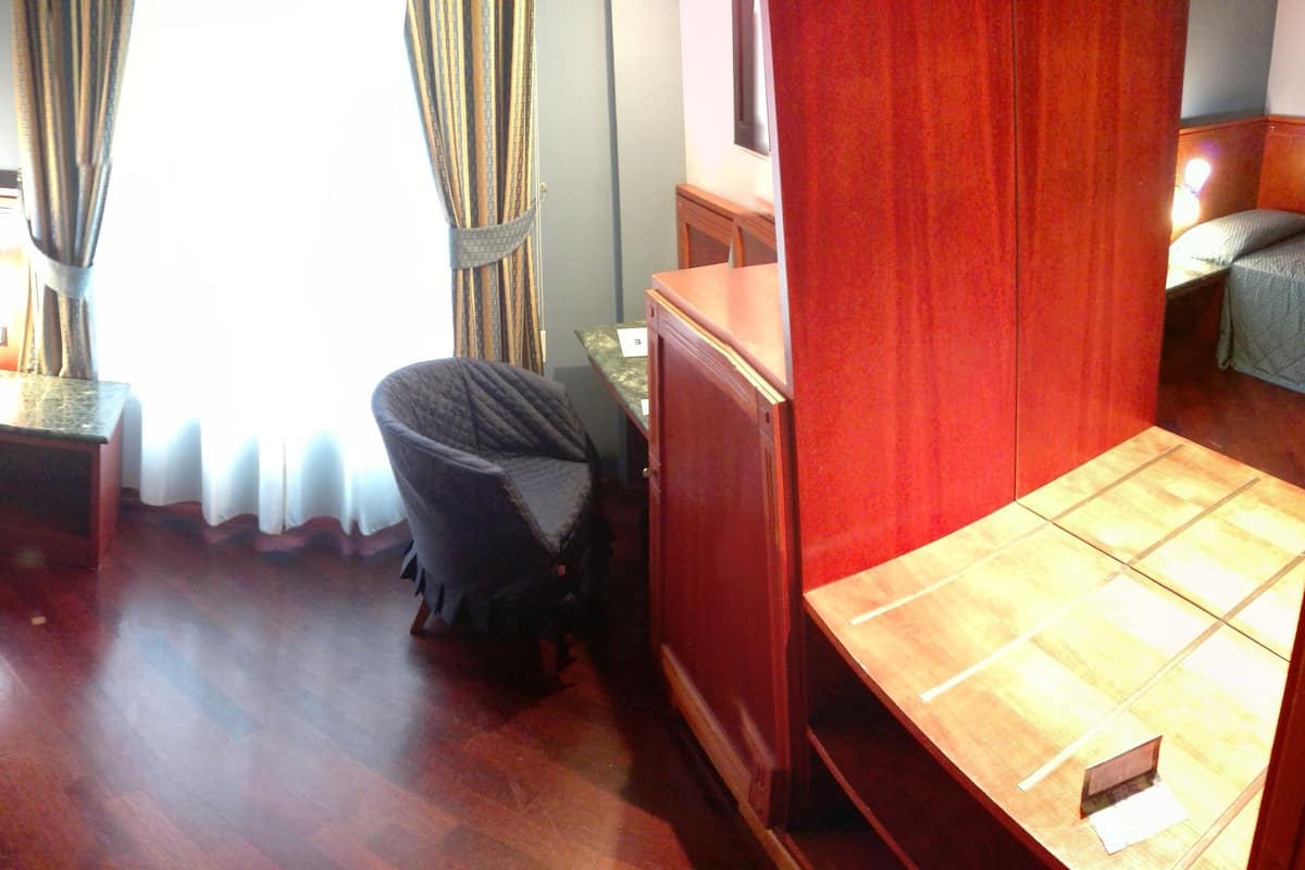A hotel room with two single beds, a small table, a chair, a wooden cabinet, and a view of the outdoors.
