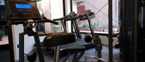 Un gimnasio con una cinta de correr, banco de pesas y una pantalla digital.