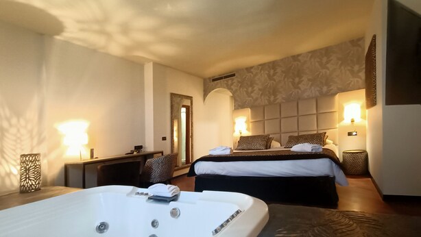 A hotel room with a large bathtub, two beds with headboards, bedside lamps, a mirror, and a small desk. - Hotel Michelangelo Palace (Terni)