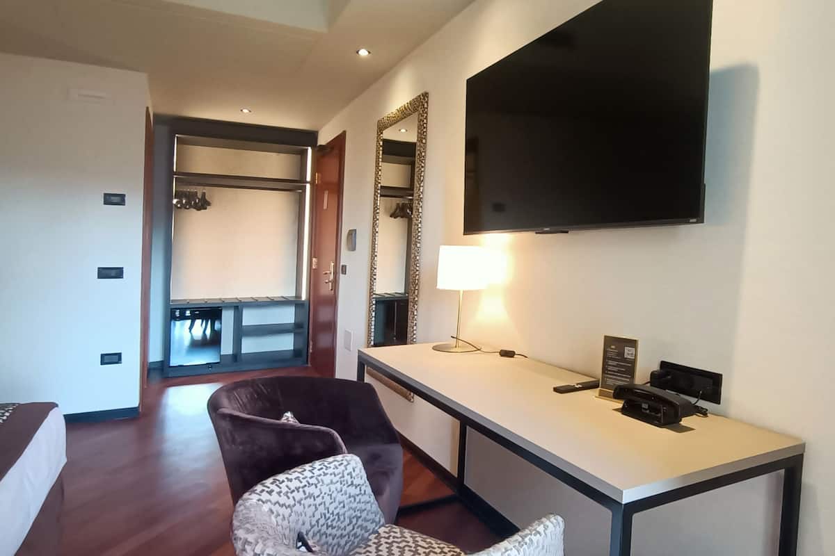 A hotel room with a bed, a desk, a TV, a chair, and a trash can.