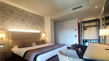 Une chambre d’hôtel avec un grand lit, une chaise, une table et un mur orné d’un motif de feuilles.