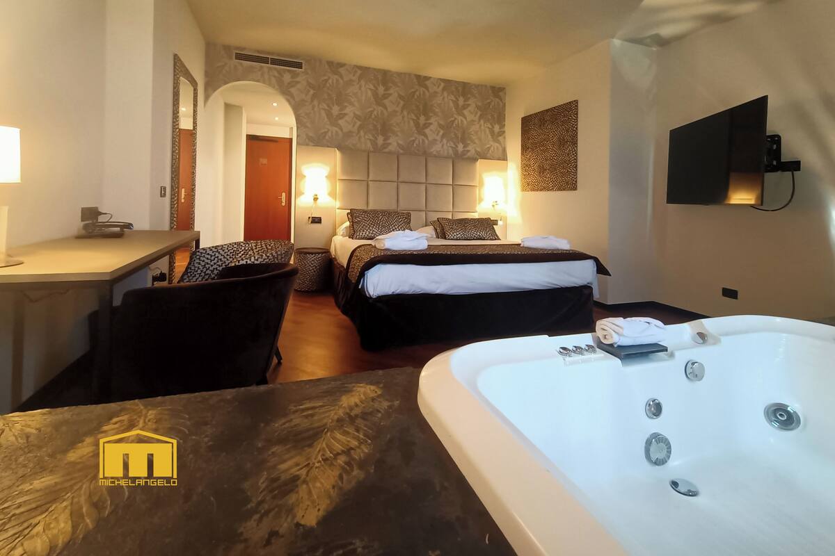 A hotel room with two beds, a desk, a chair, a large bathtub, and a wall-mounted TV.
