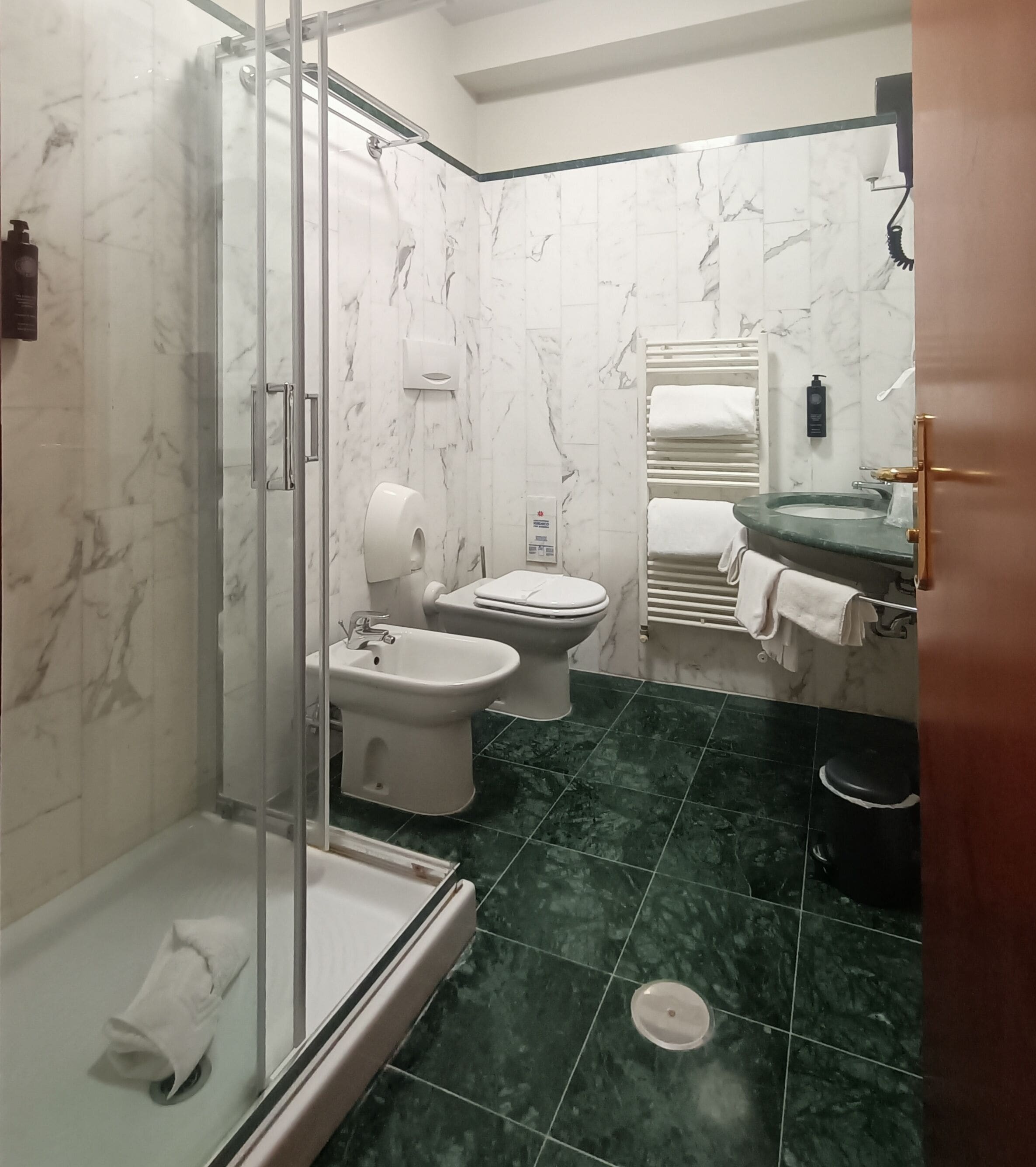 A bathroom with a glass shower enclosure, a bidet, a toilet, and a sink with a mirror.