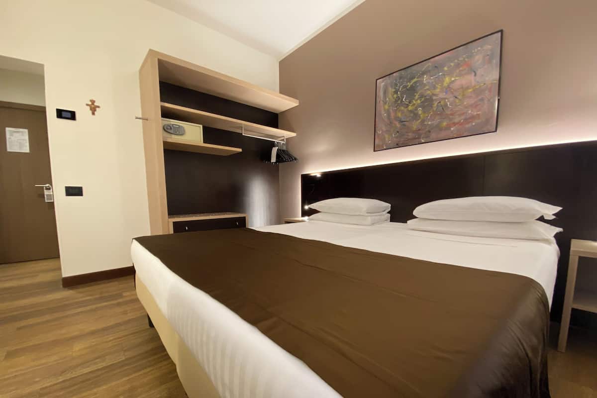 Habitación de hotel con una cama grande, un armario con estantes, una mesita de noche y un cuadro en la pared.
