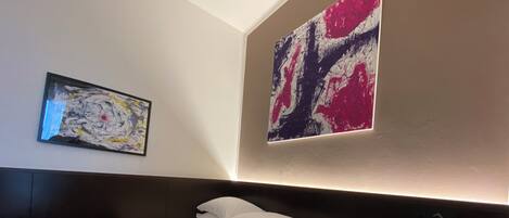 Habitación de hotel con una cama, una mesita de noche y dos cuadros abstractos en las paredes.