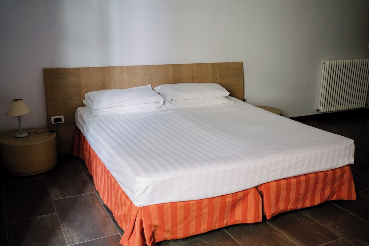 Una cama bien hecha con tablero de madera, falda a rayas rojas y ropa de cama blanca.