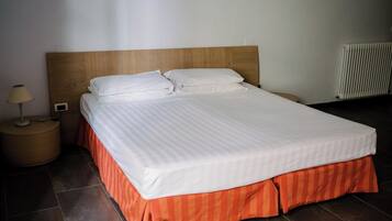 Una cama bien hecha con tablero de madera, falda a rayas rojas y ropa de cama blanca.