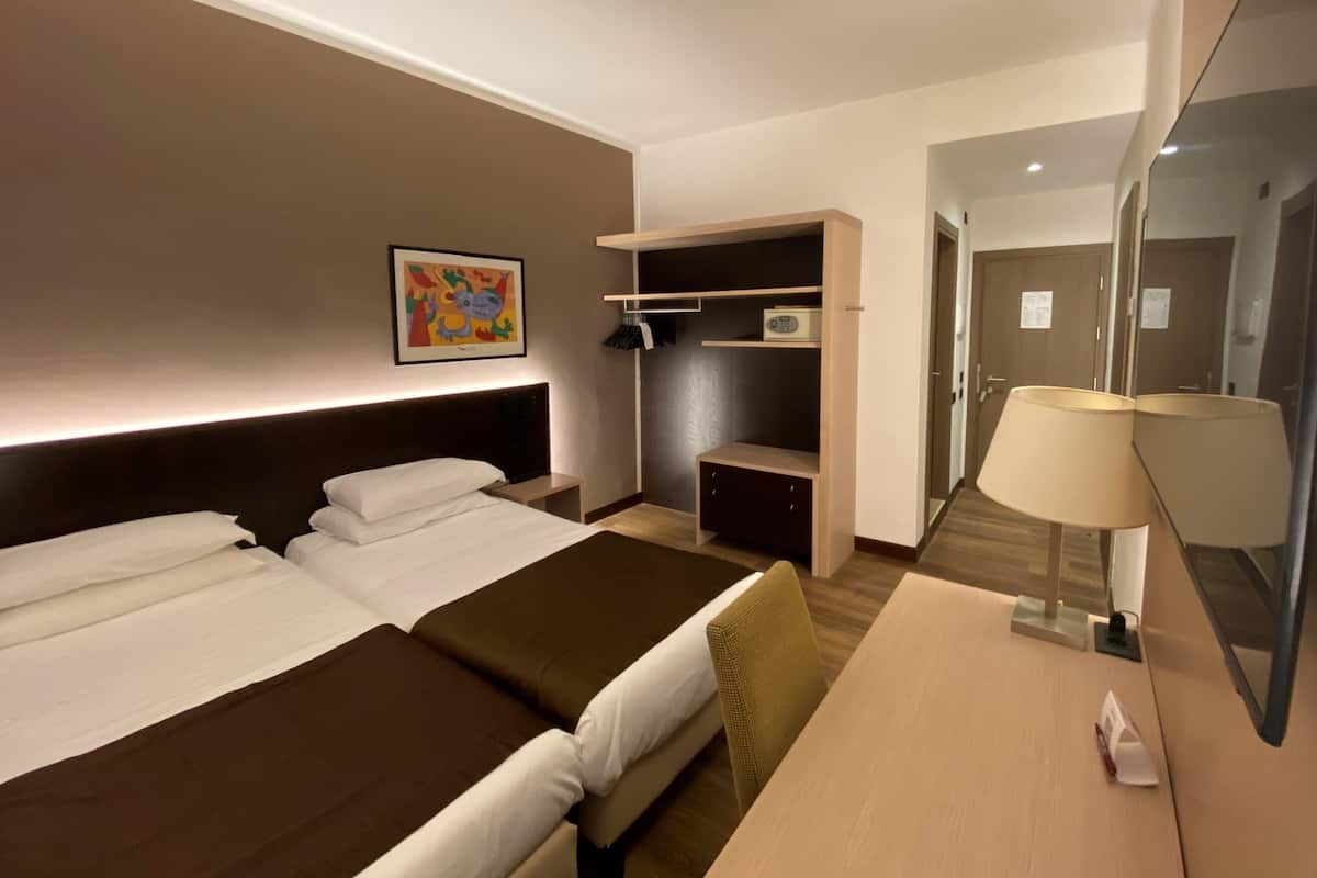 Una habitación de hotel con cama, escritorio, espejo, armario y un cuadro en la pared.