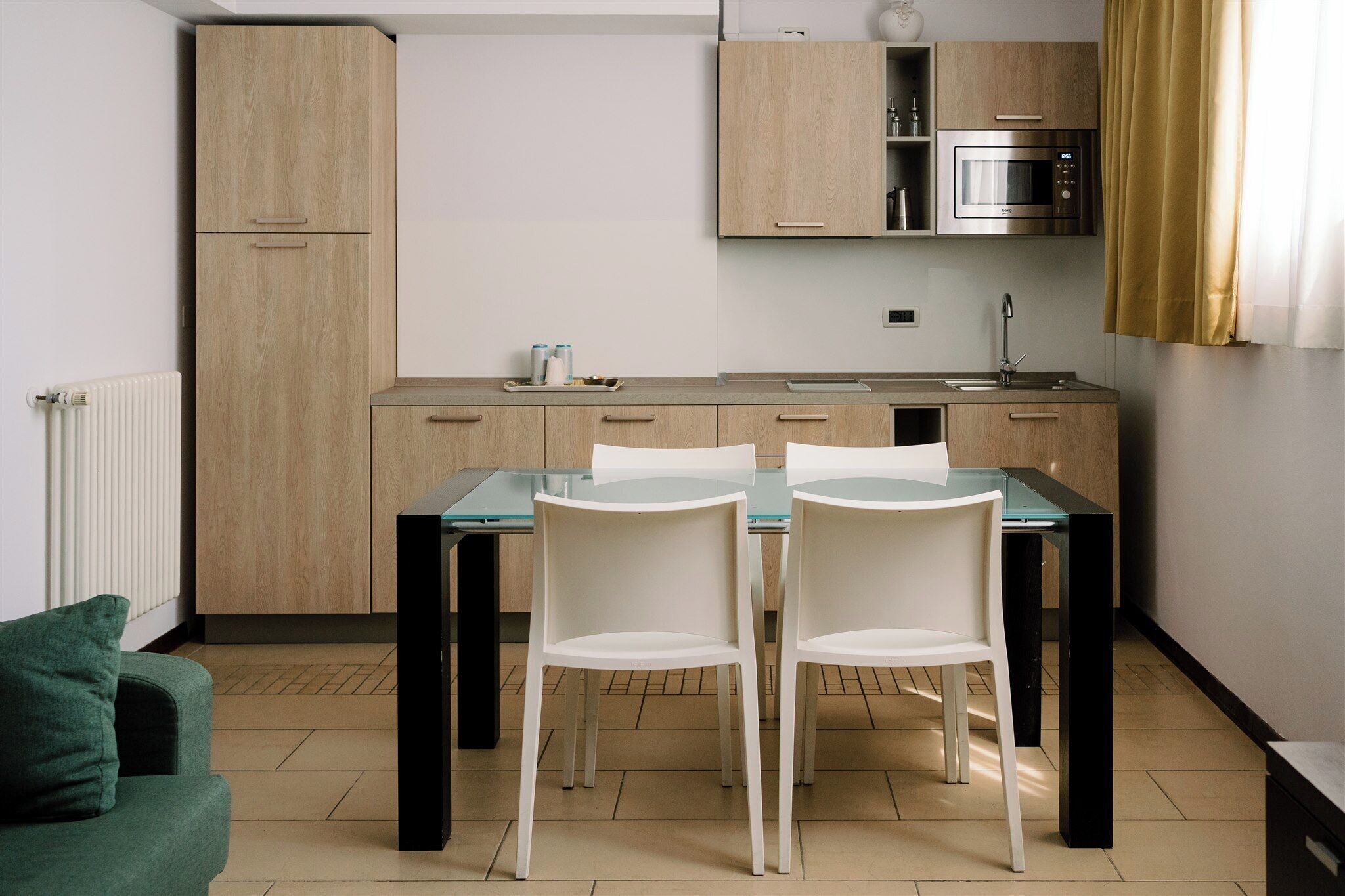 A modern kitchen with wooden cabinets, a built-in microwave, and a glass dining table with white chairs.