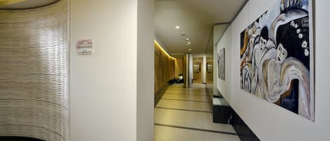 Un couloir d’hôtel avec un mur aux motifs ondulés, un sol carrelé et des œuvres d’art accrochées aux murs.