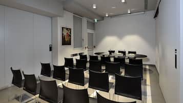 Une salle de conférence avec une table ronde et des chaises noires, des murs blancs et un tableau accroché au mur.