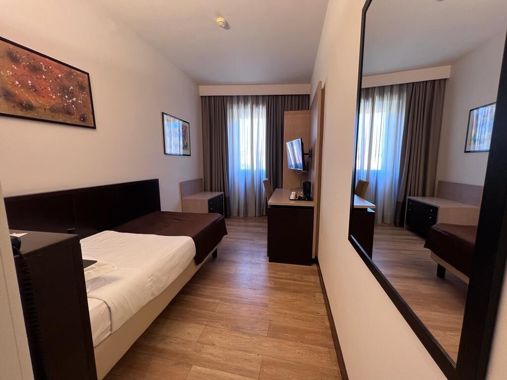 A hotel room with a bed, a desk, a TV, and a large mirror.
