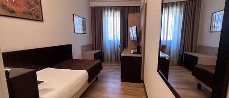 Habitación de hotel con cama, escritorio, televisor y un espejo grande.