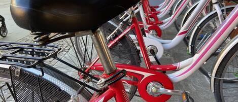 Una bicicleta roja con asiento negro y una canasta, estacionada en la acera.