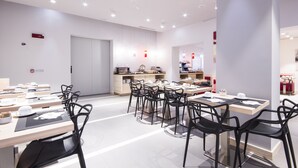 A modern dining area with multiple tables and chairs, a kitchen area, and a visible door. - Hotel Carlton (Ferrara)