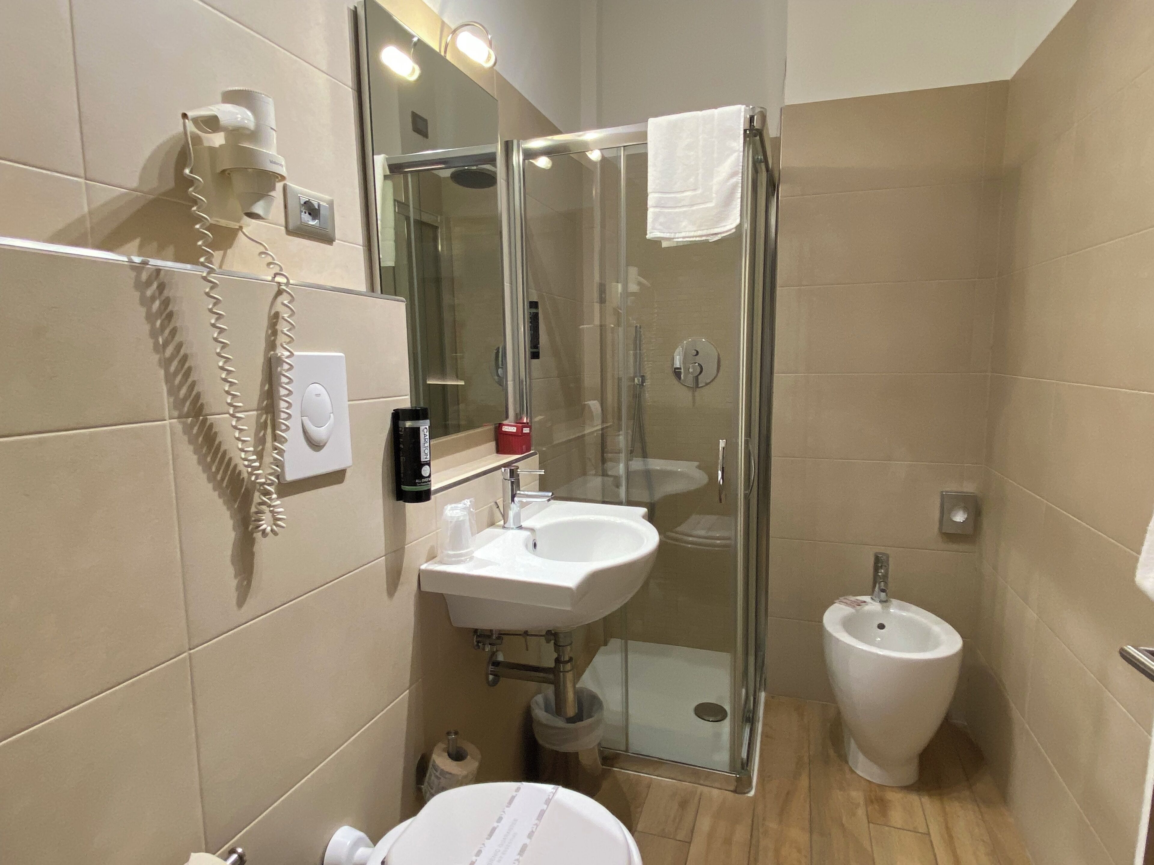 A compact bathroom with a glass shower enclosure, a white sink, a bidet, and a toilet.