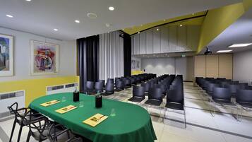 A conference room with a green table, black chairs, and a projector screen.
