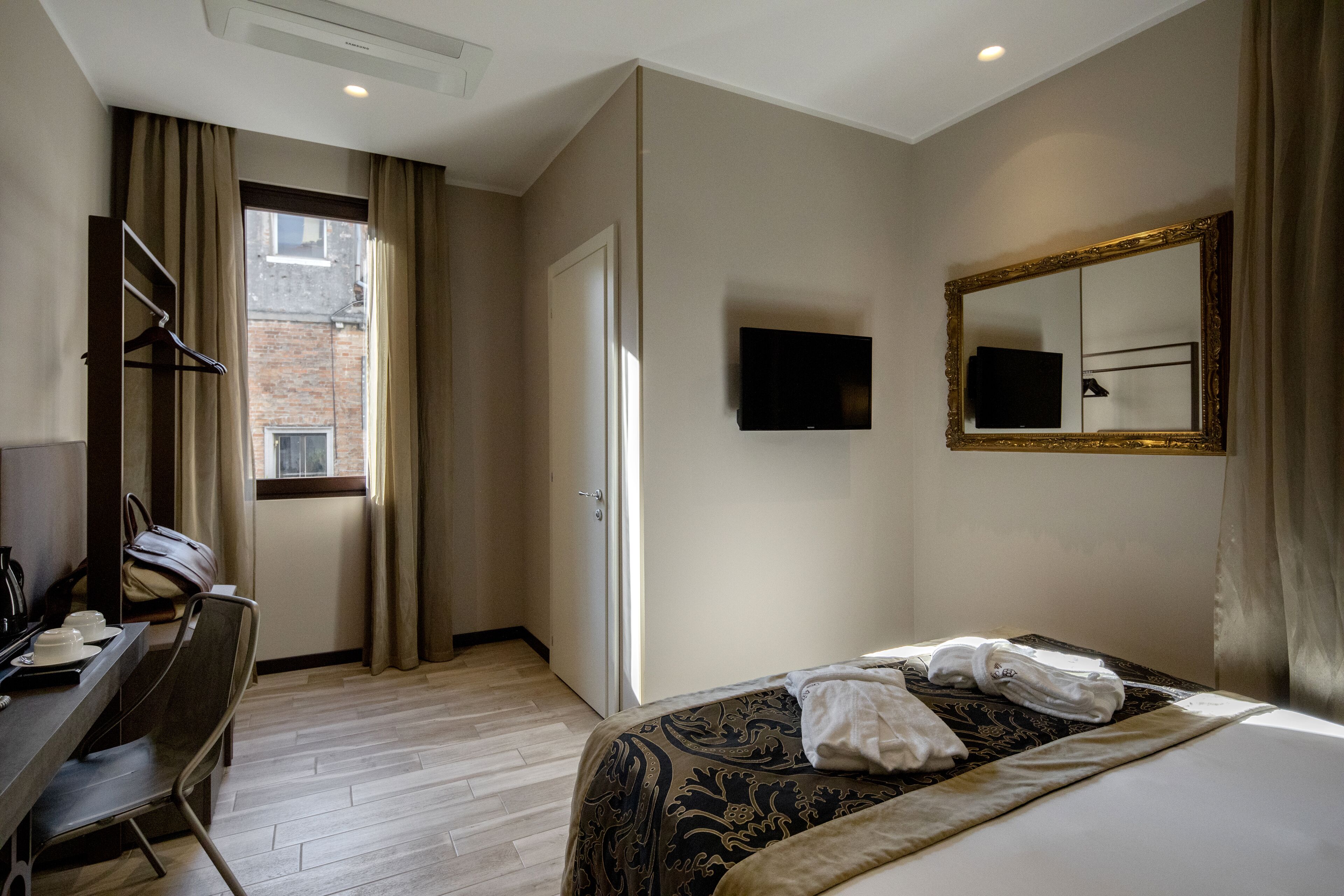 Habitación de hotel con cama, escritorio, silla, televisor y ventana con cortinas.