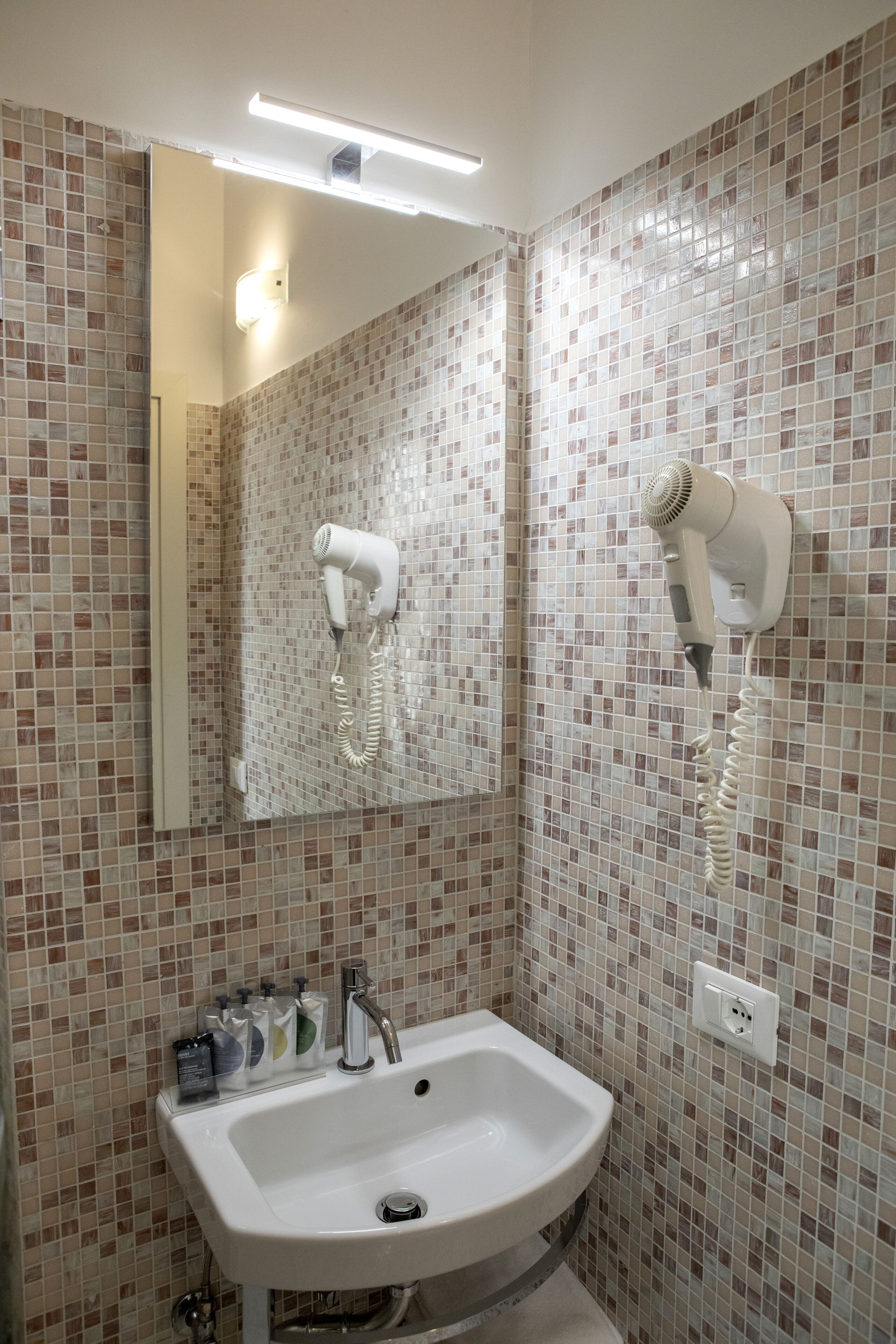 A bathroom with a sink, mirror, and hair dryer mounted on the wall.