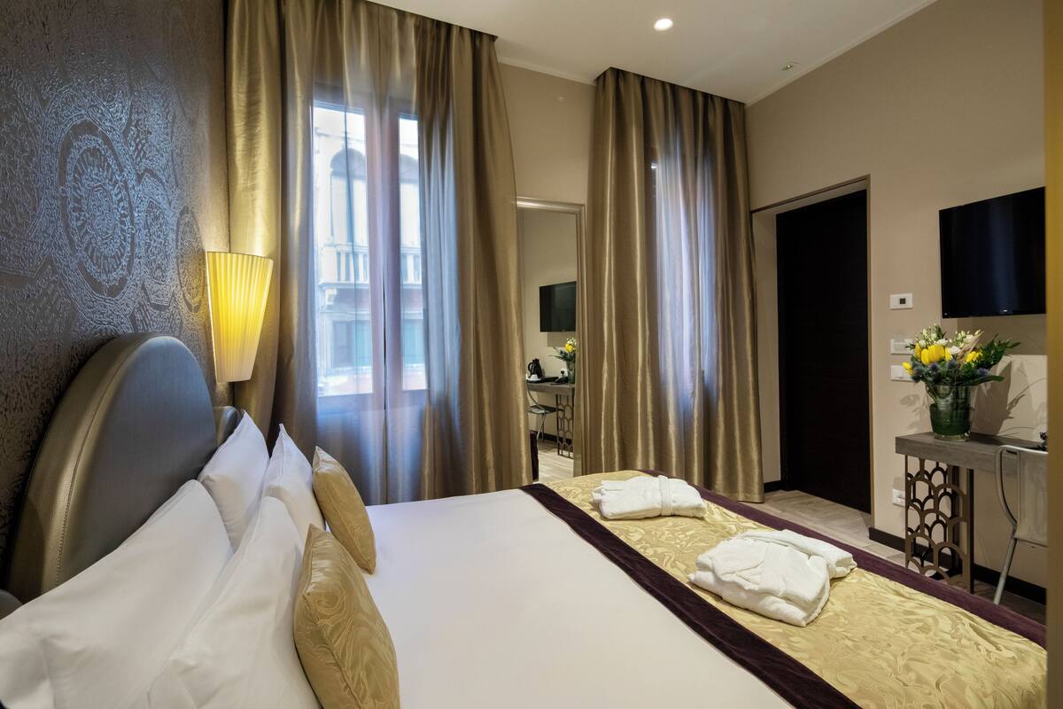 Hotelkamer met een groot bed, een bureau met een flatscreen televisie en uitzicht op de stad door grote ramen.