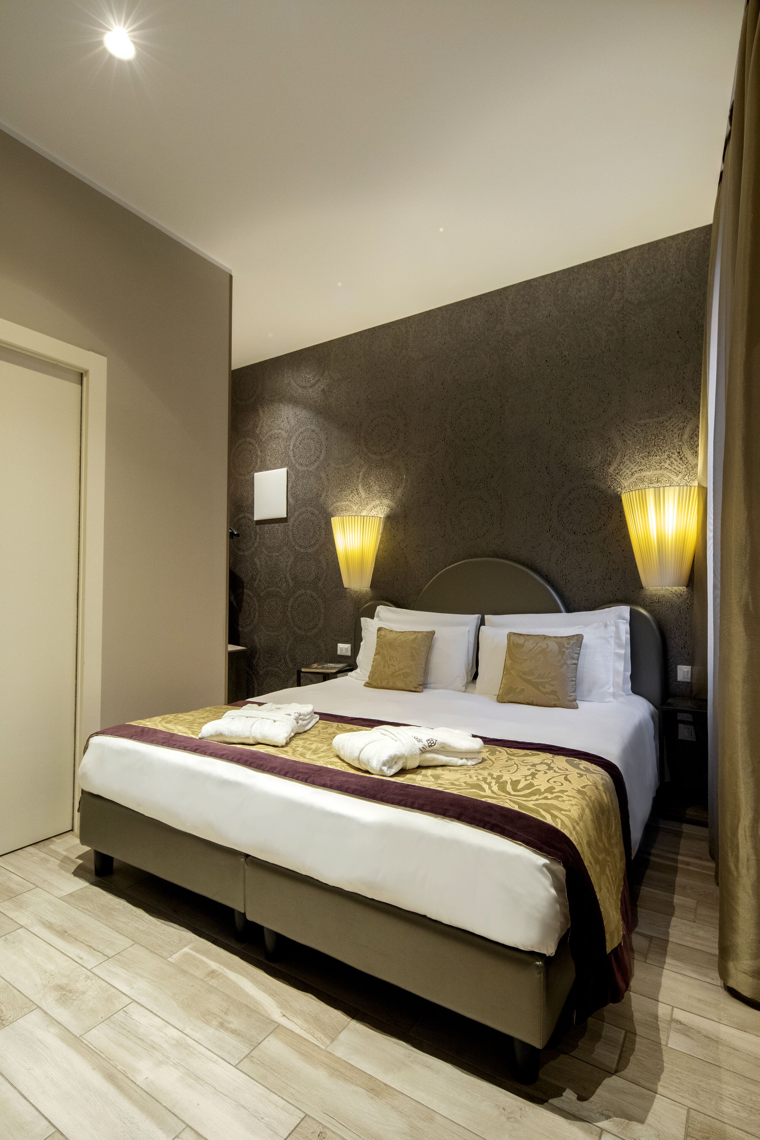 A hotel room with a large bed, two bedside lamps, and a patterned wall.