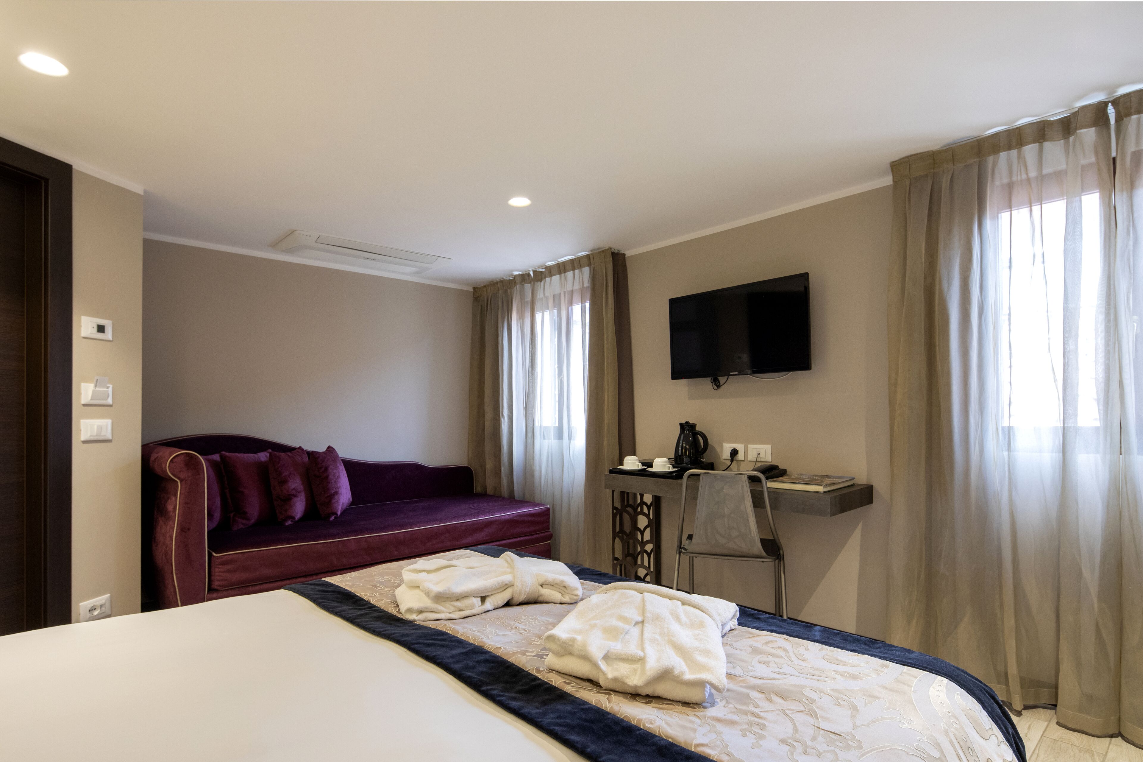 A hotel room with a bed, a desk, a chair, a TV, and a sofa.