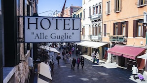 Ein Hotel-Schild mit der Aufschrift 'HOTEL 'Alle Gugliese' in einem belebten Fußgängerbereich mit traditioneller Architektur.