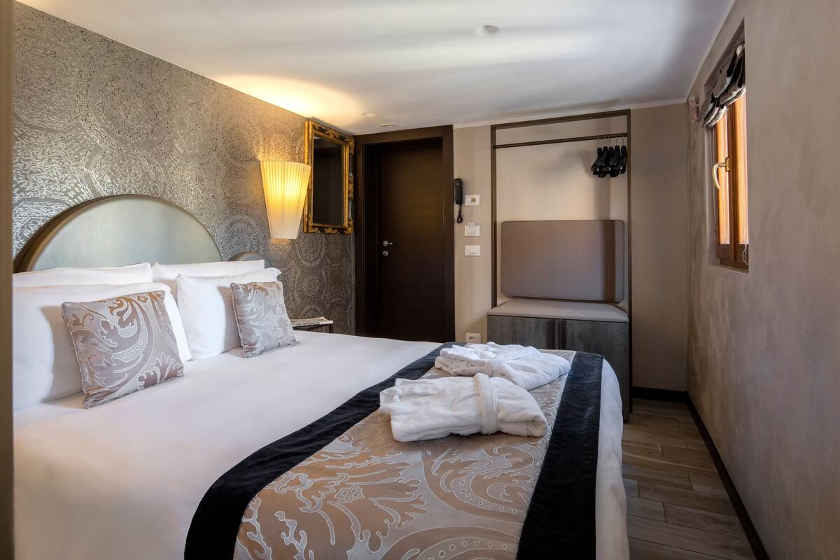 Een hotelkamer met een groot bed, een nachtkastje, een lamp, een kledingkast en een raam.