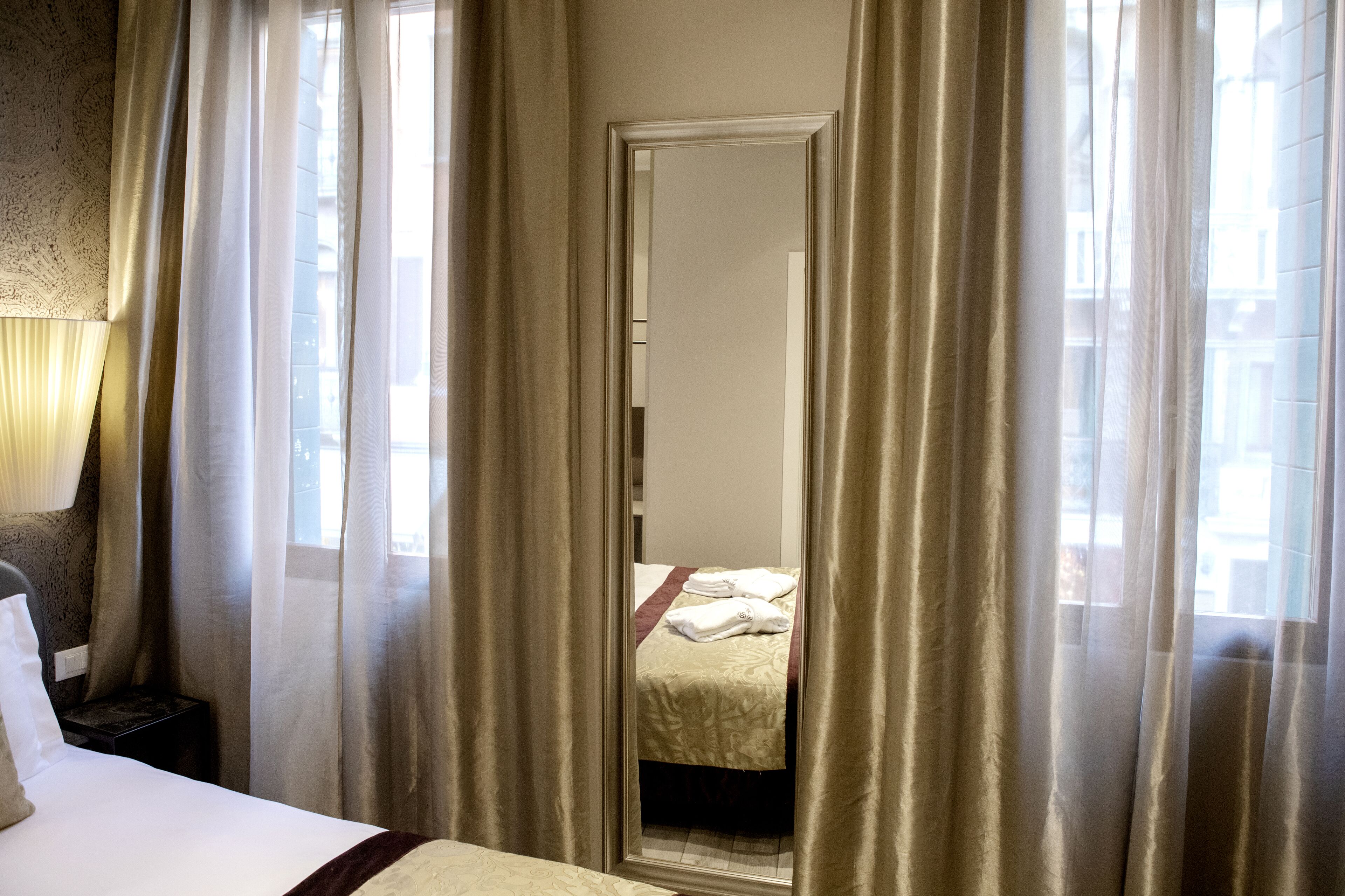 A hotel room with a bed, a nightstand, and a mirror reflecting a bed with towels.
