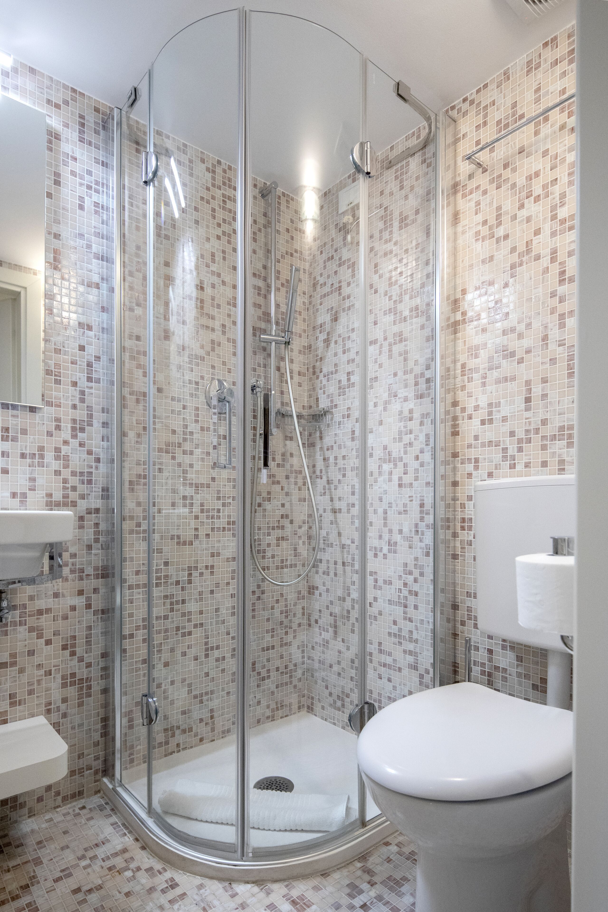 Ein modernes Badezimmer mit einer gläsernen Duschkabine, einer weißen Toilette und einem Waschbecken mit Spiegel.