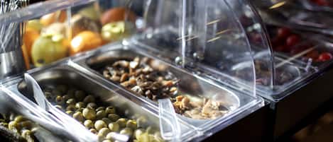 Un bufé con diversas opciones de comida, incluyendo frutas, nueces y aceitunas.