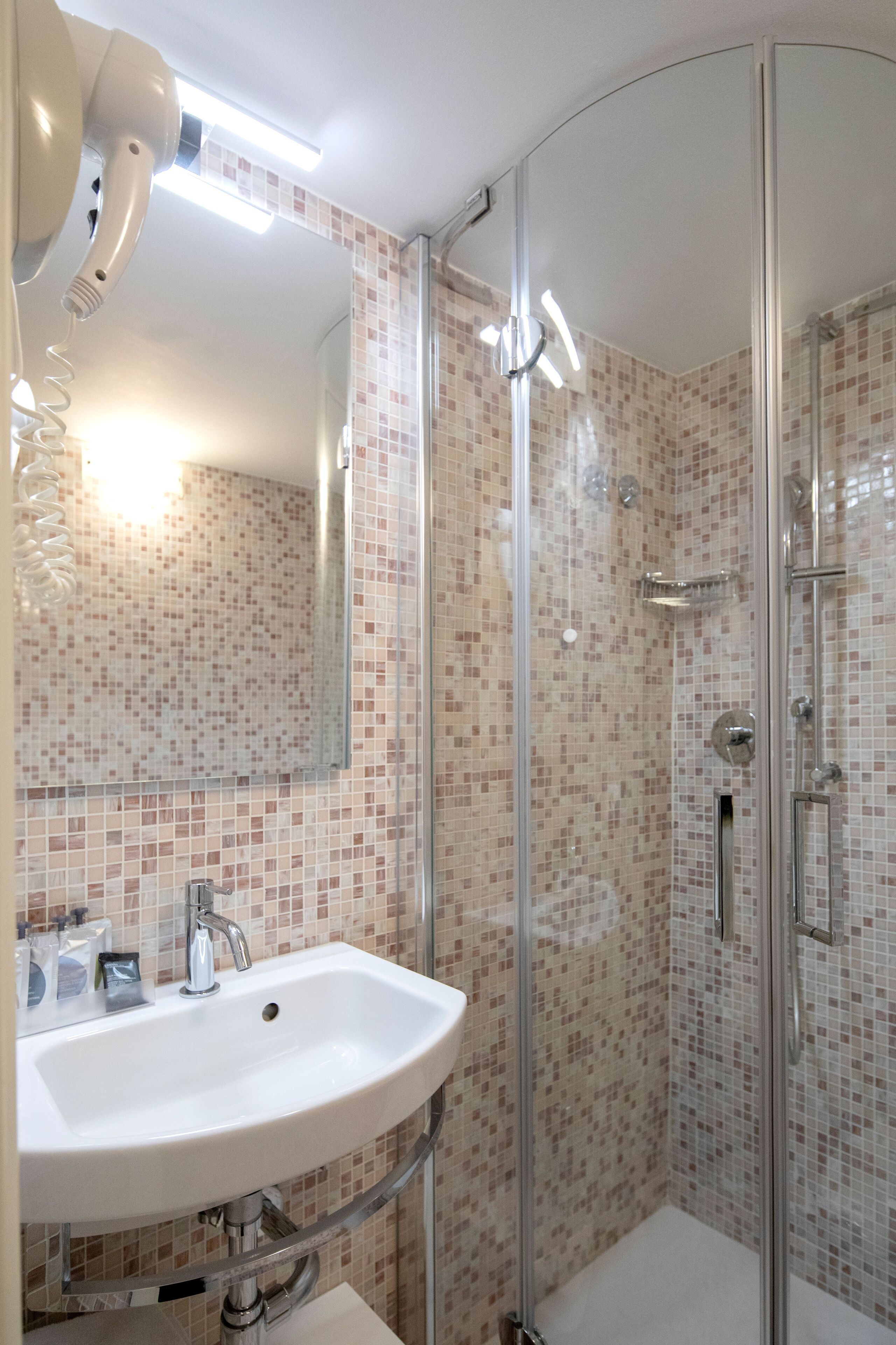 Un baño moderno con ducha envuelta en vidrio, un lavabo blanco y un salpicadero de azulejos.