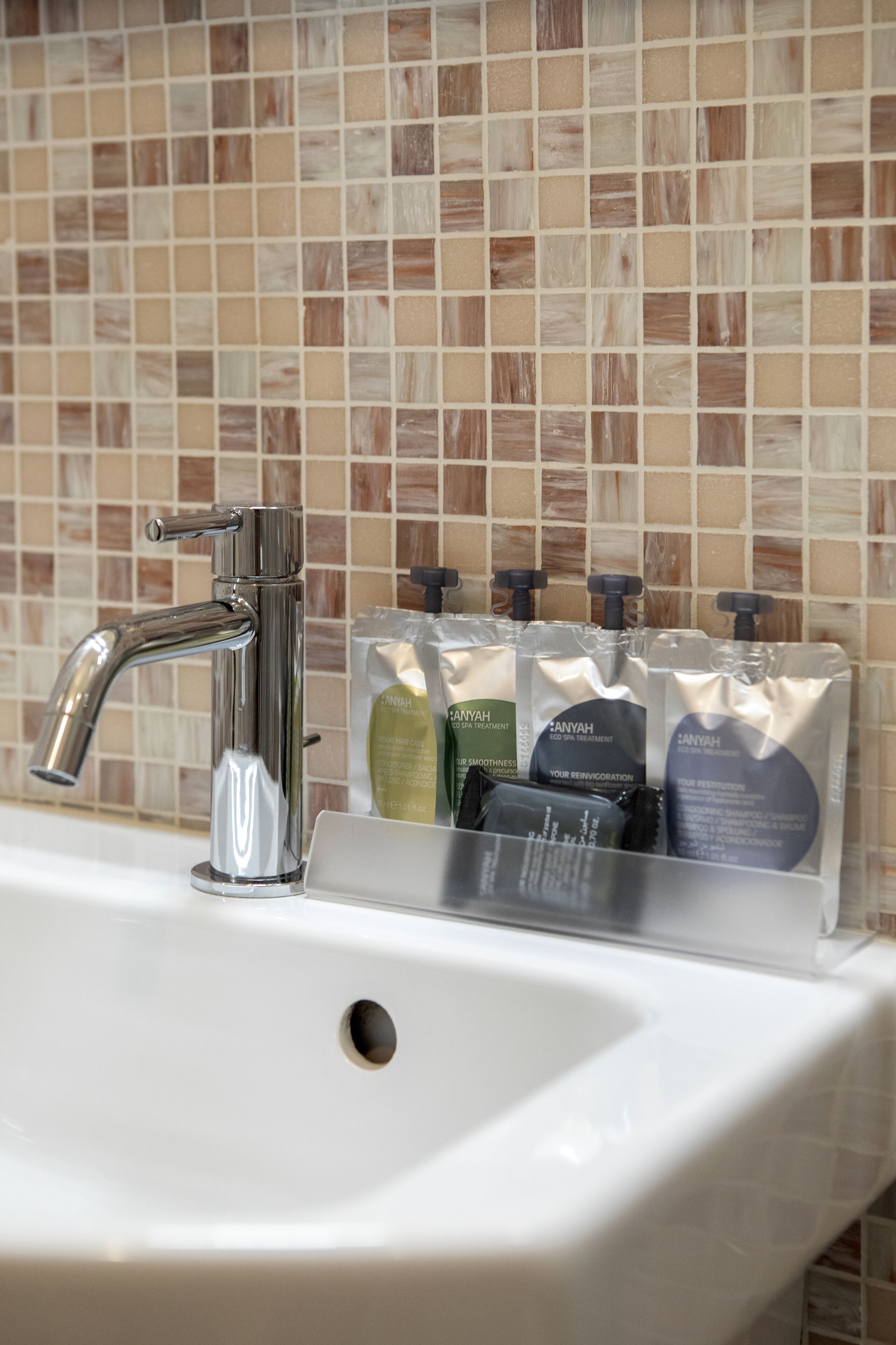 A bathroom sink with a chrome faucet and a soap dispenser holder containing multiple soap bottles.