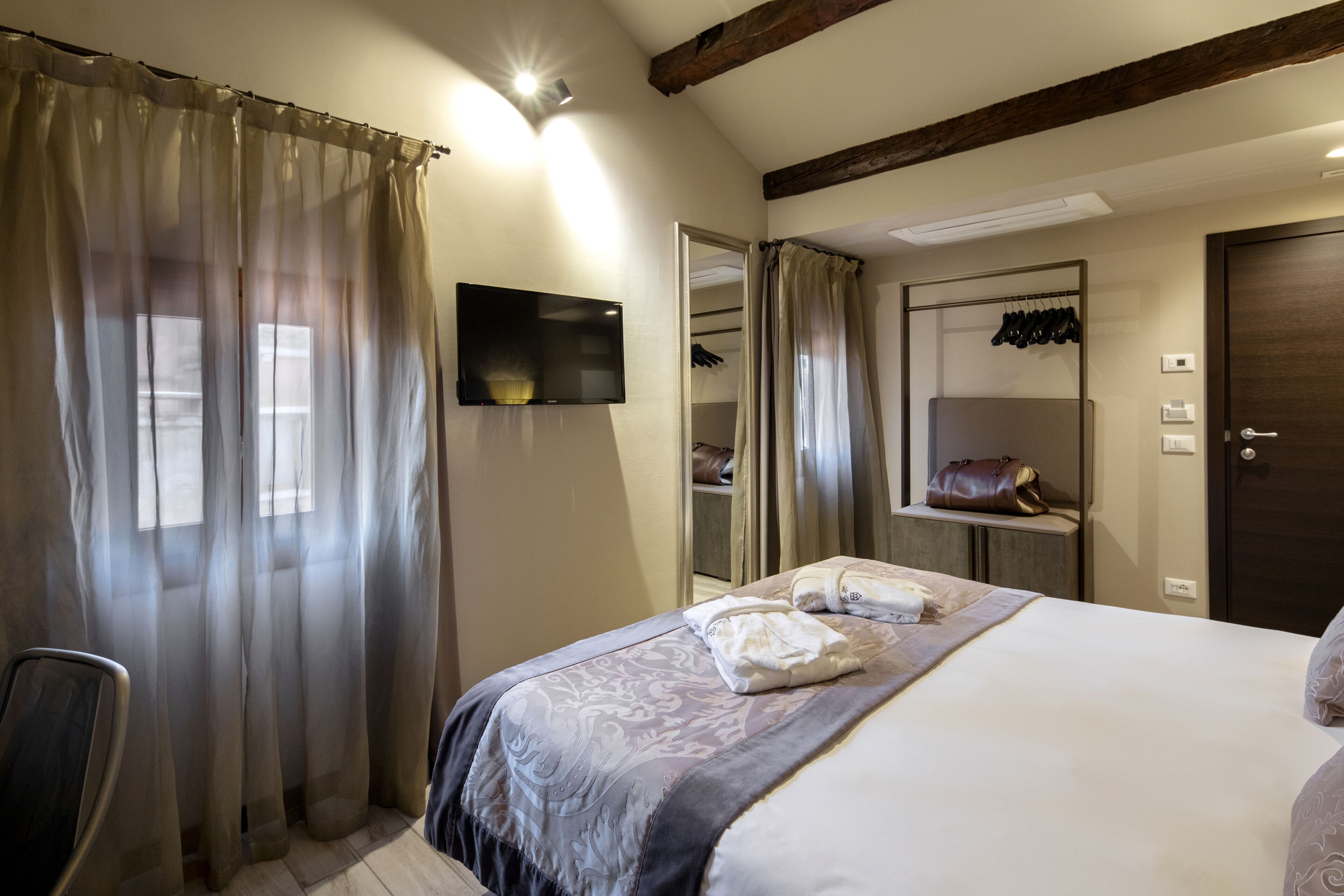 Un dormitorio con una cama, televisor, espejo, perchero y puerta.