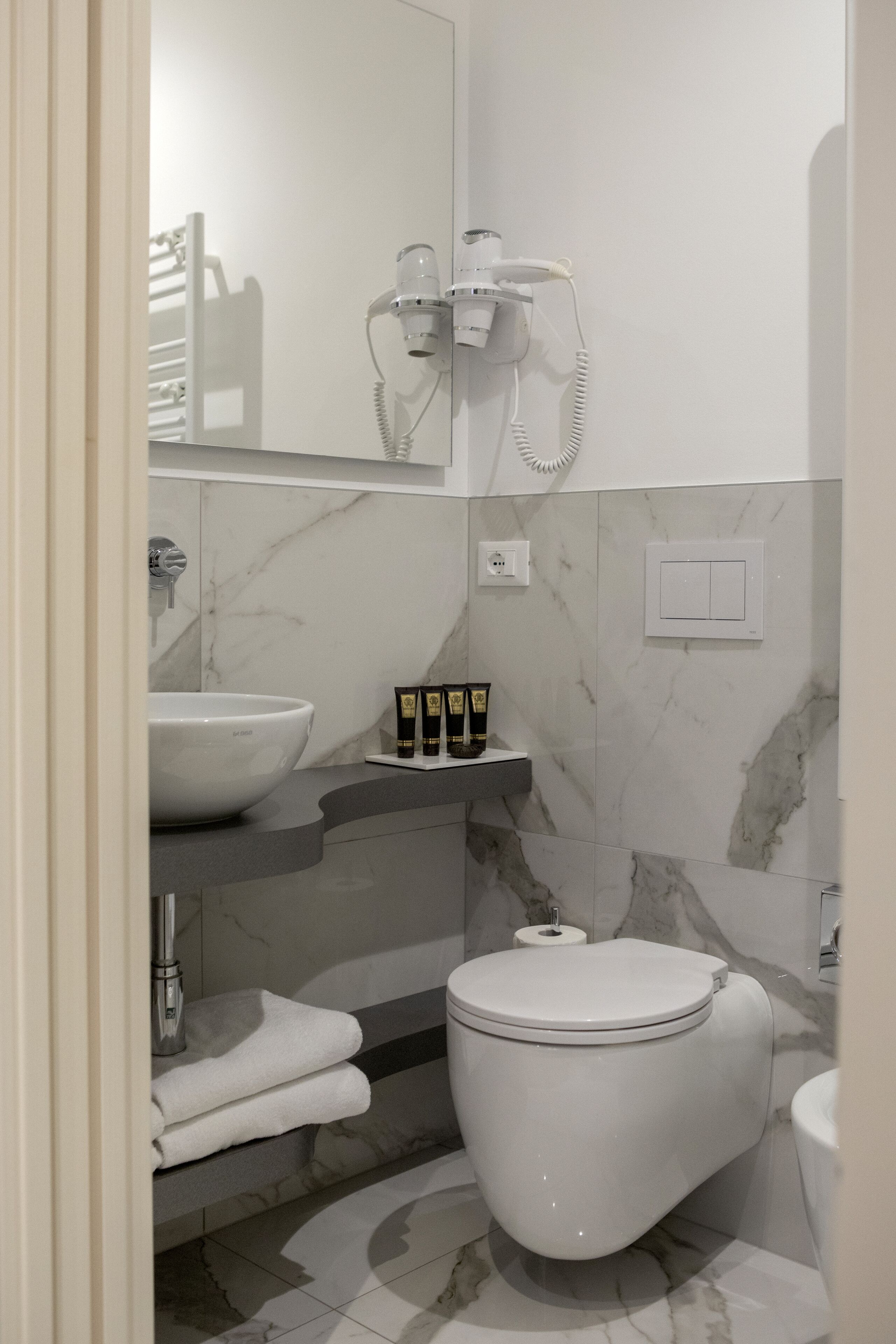 A modern bathroom with a white toilet, a sink, and a hairdryer mounted on the wall.