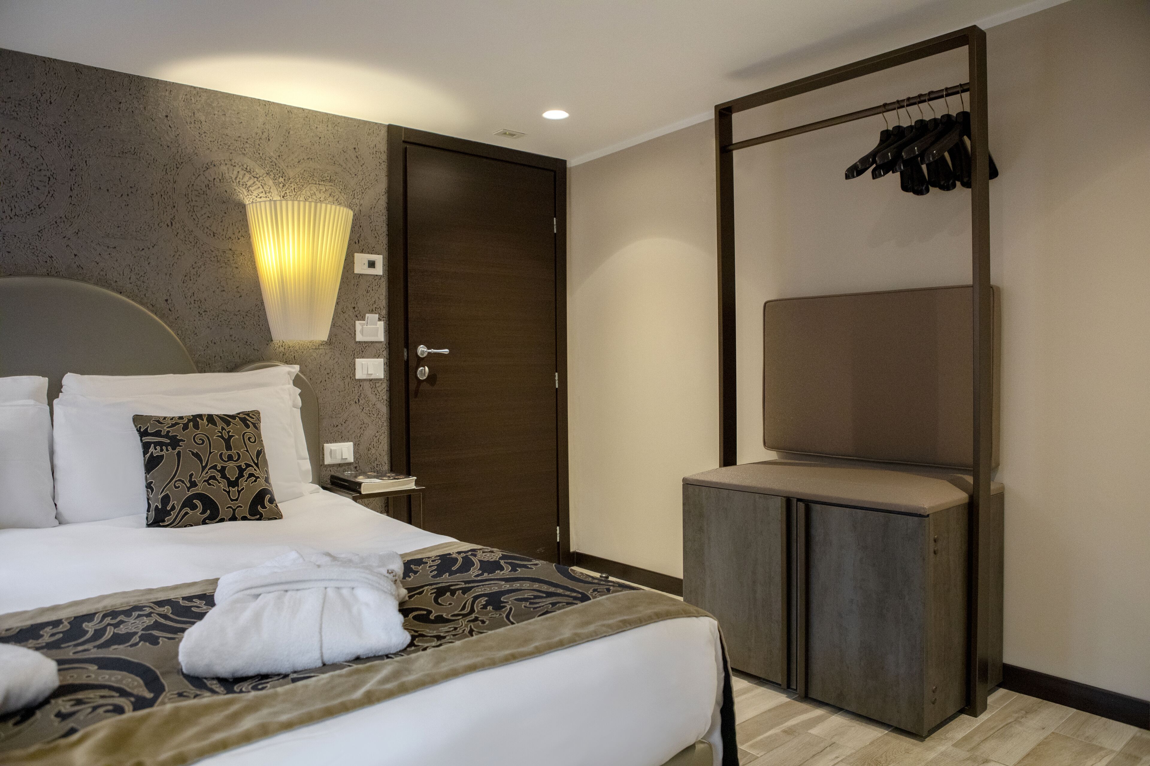 A hotel room with a large bed, a bedside table, a wardrobe, a mirror, and a coat rack.
