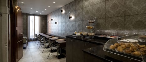 A modern kitchen with a long counter, a glass display case with pastries, and a seating area with tables and chairs.