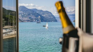 A view of a coastal area with mountains, a sailboat, and a bottle of champagne in the foreground. - Hotel Araba Fenice (Iseo)
